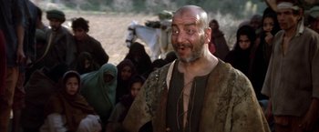 Movie still from “The Man Who Would Be King” (1975), directed by John Huston – A man with a beard is standing in front of a group of people; Medium shot, Low angle