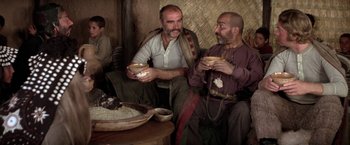 Movie still from “The Man Who Would Be King” (1975), directed by John Huston – A couple of men sitting next to each other holding bowls; Medium shot, Low angle