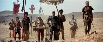 Movie still from “The Man Who Would Be King” (1975), directed by John Huston – A group of people standing in the desert; Wide shot, Low angle