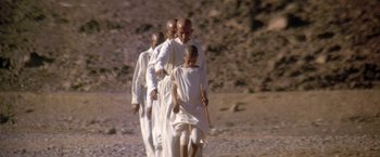 Movie still from “The Man Who Would Be King” (1975), directed by John Huston – A group of people walking on a dirt road; Wide shot, Low angle