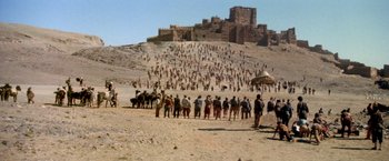 Movie still from “The Man Who Would Be King” (1975), directed by John Huston – A large group of people walking up a hill in the desert; Extreme Wide shot, High angle