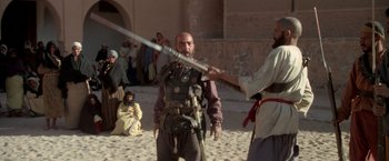 Movie still from “The Man Who Would Be King” (1975), directed by John Huston – A man holding a sword in front of another man; Medium shot, Over the shoulder angle