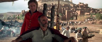 Movie still from “The Man Who Would Be King” (1975), directed by John Huston – A man in a red and white shirt sitting next to another man in a red and white shirt; Medium shot, Low angle