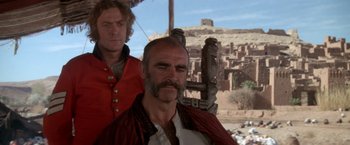 Movie still from “The Man Who Would Be King” (1975), directed by John Huston – A man in a red shirt and a man in a red shirt; Medium shot, Low angle