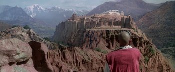 Movie still from “The Man Who Would Be King” (1975), directed by John Huston – A man standing on top of a cliff looking at a mountain; Extreme Wide shot, High angle