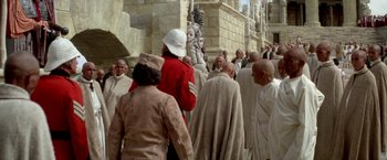 Movie still from “The Man Who Would Be King” (1975), directed by John Huston – A group of people standing in front of a stone building; Wide shot, High angle