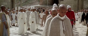 Movie still from “The Man Who Would Be King” (1975), directed by John Huston – A large group of men in white robes walking down a street; Wide shot, High angle