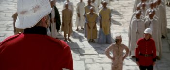 Movie still from “The Man Who Would Be King” (1975), directed by John Huston – A group of people in costumes walking down a street; Close Up shot, Over the shoulder angle
