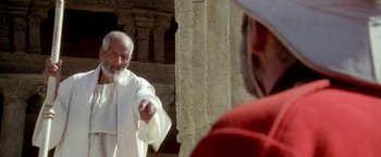Movie still from “The Man Who Would Be King” (1975), directed by John Huston – An old man wearing a white robe pointing at a woman wearing a red dress; Medium shot, Over the shoulder angle
