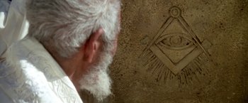 Movie still from “The Man Who Would Be King” (1975), directed by John Huston – An old man with a white beard is looking at a masonic symbol; Extreme Close Up shot, Overhead angle