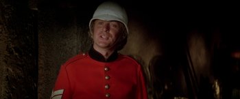 Movie still from “The Man Who Would Be King” (1975), directed by John Huston – A man wearing a red uniform and a white hat; Close Up shot, Low angle