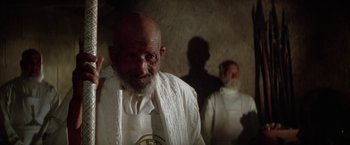 Movie still from “The Man Who Would Be King” (1975), directed by John Huston – A man with a beard and a white shirt is standing in front of another man with a beard; Close Up shot, Low angle