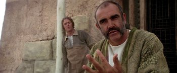 Movie still from “The Man Who Would Be King” (1975), directed by John Huston – Two men standing next to each other in front of a stone wall; Close Up shot, Over the shoulder angle