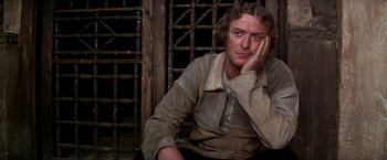 Movie still from “The Man Who Would Be King” (1975), directed by John Huston – A man sitting in front of a metal gate; Close Up shot, High angle