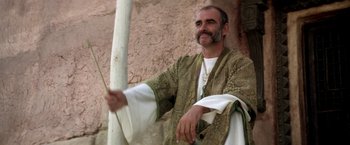 Movie still from “The Man Who Would Be King” (1975), directed by John Huston – A man in a robe holding a white stick; Medium shot, Low angle