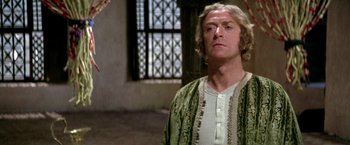 Movie still from “The Man Who Would Be King” (1975), directed by John Huston – A man with blonde hair wearing a green robe; Close Up shot, Over the shoulder angle