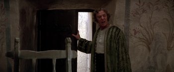 Movie still from “The Man Who Would Be King” (1975), directed by John Huston – A man in a green robe is standing in front of an open door; Medium shot, Low angle