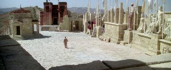 Movie still from “The Man Who Would Be King” (1975), directed by John Huston – A man walking across a stone walkway in a desert; Extreme Wide shot, High angle