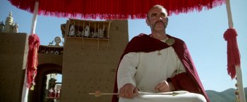 Movie still from “The Man Who Would Be King” (1975), directed by John Huston – An old man dressed as a roman centurion holding an arrow; Medium shot, Low angle