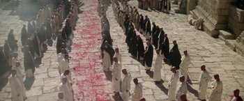 Movie still from “The Man Who Would Be King” (1975), directed by John Huston – A large group of people walking down a street; Extreme Wide shot, High angle