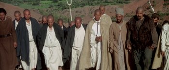 Movie still from “The Man Who Would Be King” (1975), directed by John Huston – A group of men standing next to each other on top of a hill; Wide shot, High angle
