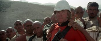 Movie still from “The Man Who Would Be King” (1975), directed by John Huston – A group of men standing next to each other in a field; Medium shot, Over the shoulder angle