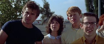 Movie still from “American Graffiti” (1973), directed by George Lucas – A group of young people standing next to each other; Close Up shot, Low angle