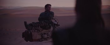 Movie still from “The Mandalorian” (2019), created by Jon Favreau – A man sitting on top of a motorcycle in the desert at night; Wide shot, Over the shoulder angle