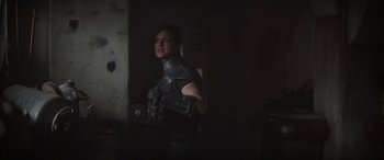Movie still from “The Mandalorian” (2019), created by Jon Favreau – A woman standing in a dark room holding a gun; Medium shot, Over the shoulder angle