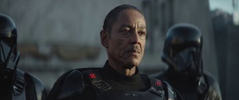 Movie still from “The Mandalorian” (2019), created by Jon Favreau – An older man in a black outfit looking at the camera; Close Up shot, Over the shoulder angle