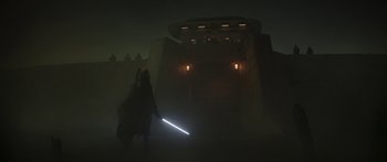Movie still from “The Mandalorian” (2019), created by Jon Favreau – A person holding a lightsaber while standing in the dark; Extreme Wide shot, Low angle