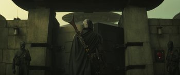 Movie still from “The Mandalorian” (2019), created by Jon Favreau – A man in a helmet and a cape holding a gun; Wide shot, Low angle