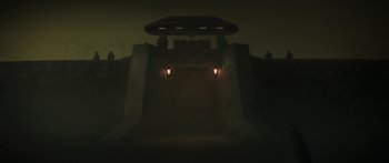 Movie still from “The Mandalorian” (2019), created by Jon Favreau – A dark picture of a building with lights on the outside; Extreme Wide shot, Low angle