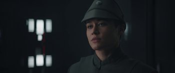 Movie still from “The Mandalorian” (2019), created by Jon Favreau – A man wearing a green uniform and a hat; Close Up shot, Over the shoulder angle