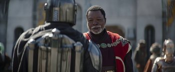 Movie still from “The Mandalorian” (2019), created by Jon Favreau – A black man in a red and black suit and a black man in a black and red suit; Close Up shot, Over the shoulder angle