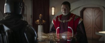 Movie still from “The Mandalorian” (2019), created by Jon Favreau – An older man wearing a red and black outfit; Medium shot, Over the shoulder angle