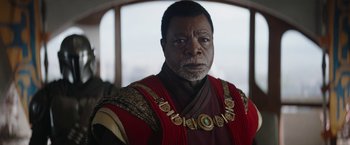 Movie still from “The Mandalorian” (2019), created by Jon Favreau – An older man wearing a red and gold outfit; Close Up shot, Over the shoulder angle
