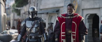 Movie still from “The Mandalorian” (2019), created by Jon Favreau – Two people dressed in costumes standing next to each other on a city street; Medium shot, Low angle