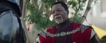 Movie still from “The Mandalorian” (2019), created by Jon Favreau – An older man wearing a red and black outfit; Close Up shot, Low angle