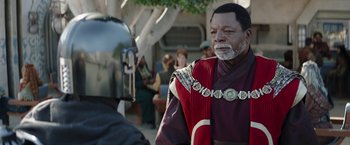 Movie still from “The Mandalorian” (2019), created by Jon Favreau – A man in a red and black outfit is talking to another man in a red and black outfit; Close Up shot, Over the shoulder angle