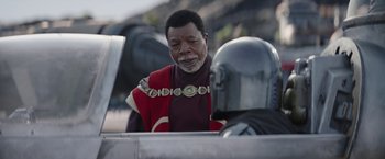 Movie still from “The Mandalorian” (2019), created by Jon Favreau – An older man wearing a red and black outfit; Close Up shot, Over the shoulder angle