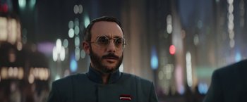 Movie still from “The Mandalorian” (2019), created by Jon Favreau – A man with a beard wearing glasses and a suit; Close Up shot, Over the shoulder angle