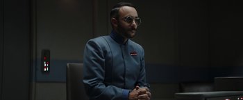 Movie still from “The Mandalorian” (2019), created by Jon Favreau – A man in a blue suit and white sunglasses; Close Up shot, Over the shoulder angle