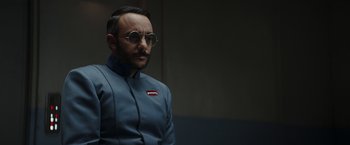 Movie still from “The Mandalorian” (2019), created by Jon Favreau – A man with a beard wearing a blue suit and round sunglasses; Close Up shot, Over the shoulder angle