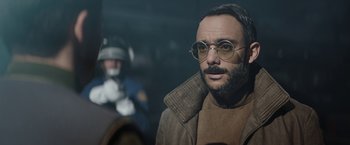 Movie still from “The Mandalorian” (2019), created by Jon Favreau – A man with a beard wearing glasses and a brown jacket; Close Up shot, Over the shoulder angle