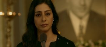 A woman with long black hair is speaking into a microphone