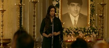 A woman standing at a microphone in front of a picture of a man