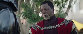 Movie still from “The Mandalorian” (2019), created by Jon Favreau – An older man wearing a red and black outfit; Close Up shot, Over the shoulder angle