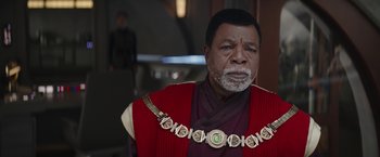 Movie still from “The Mandalorian” (2019), created by Jon Favreau – A man in a red and black outfit with a beard; Close Up shot, Over the shoulder angle