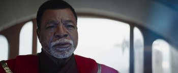 Movie still from “The Mandalorian” (2019), created by Jon Favreau – An older man wearing a red shirt and a white beard; Close Up shot, Over the shoulder angle